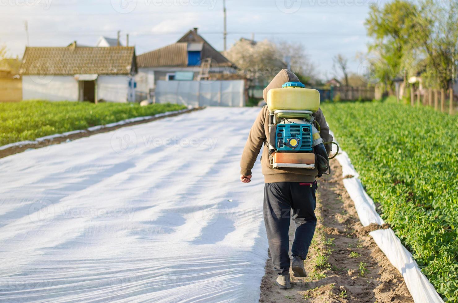 un' contadino con un' nebbia spruzzatore su il suo indietro passeggiate attraverso il azienda agricola campo. il uso di sostanze chimiche per Ritaglia protezione nel agricoltura. protezione di coltivato impianti a partire dal insetti e fungine infezioni. foto