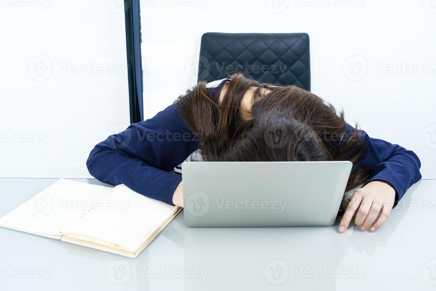 i capelli lunghi della giovane donna si addormentano sulla scrivania con il computer portatile foto