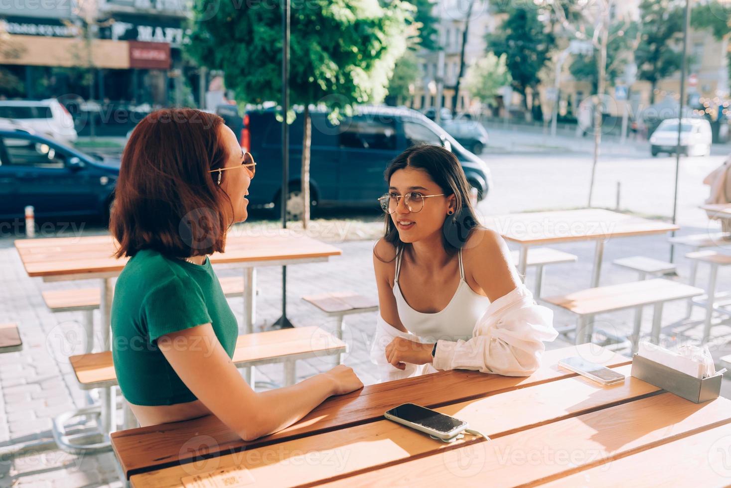 Due bella amiche parlando mentre seduta nel un' bar all'aperto foto