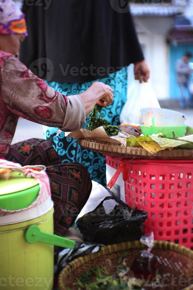 un vecchio indonesiano donna è preparazione pecel piatti per clienti. pecel cucina è un' tradizionale cibo a partire dal Indonesia foto