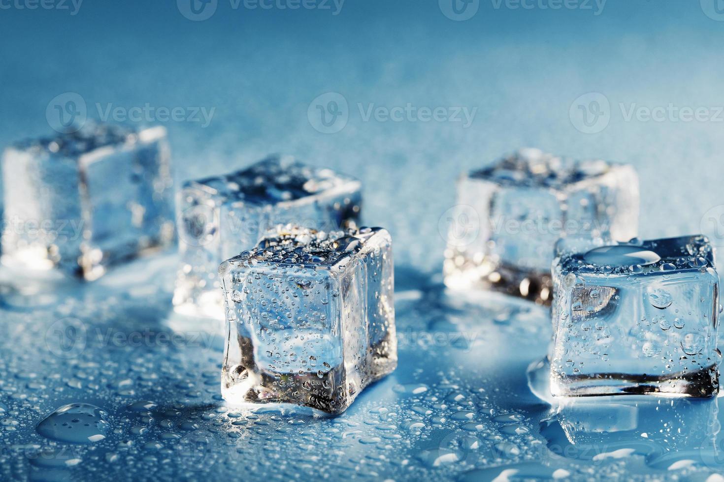 avvicinamento ghiaccio cubi con fusione acqua gocce sparpagliato su un' blu sfondo. foto