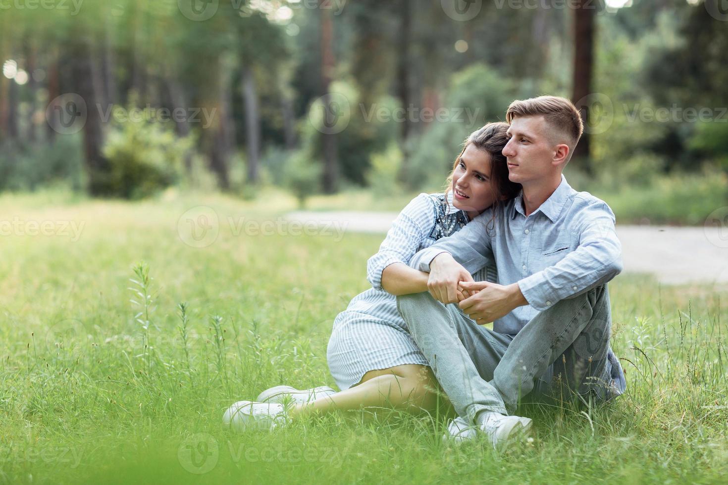 all'aperto tiro di giovane contento coppia nel amore seduta su erba su natura. uomo e donna abbracciare, luce del sole nel estate parco. contento famiglia nel il sera sole luce. il concetto vacanza foto