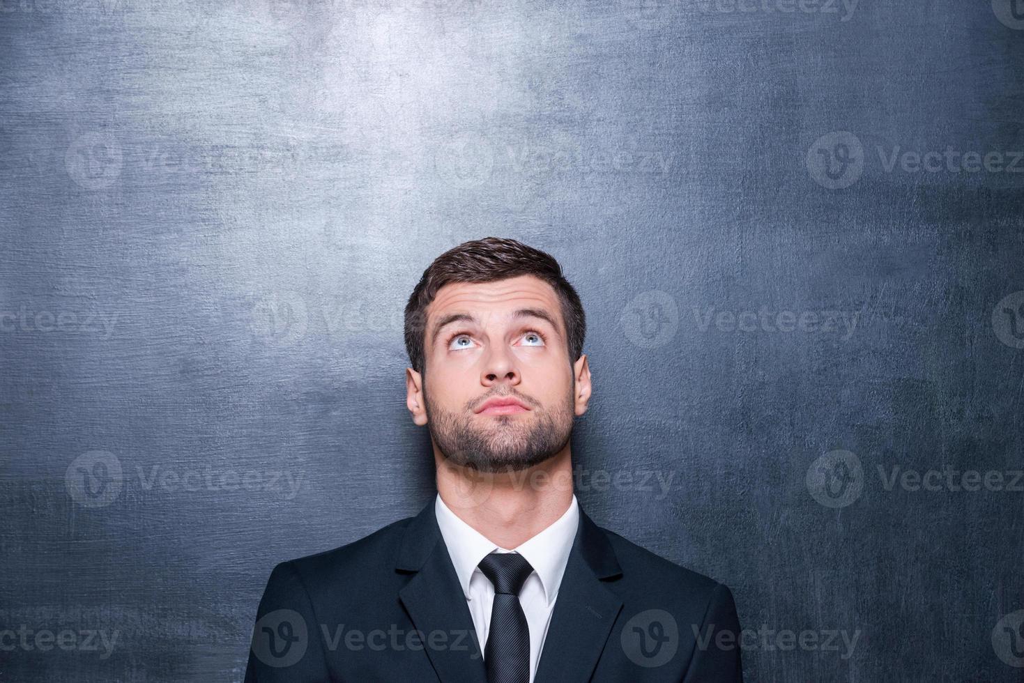 che cosa è Là bello giovane uomo nel camicia e cravatta guardare su mentre in piedi contro lavagna foto