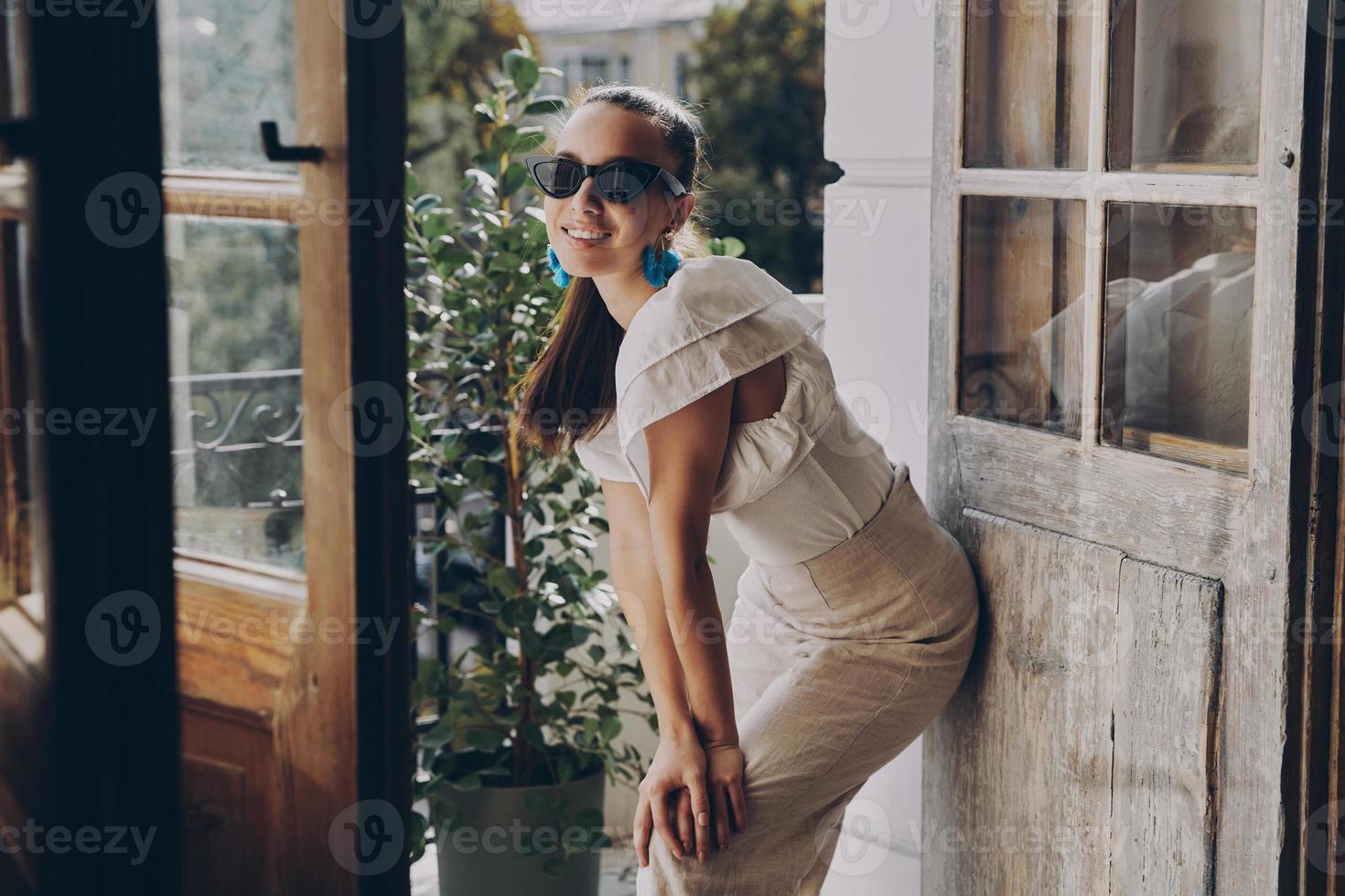 alla moda giovane donna sorridente mentre pendente a il balcone porta foto