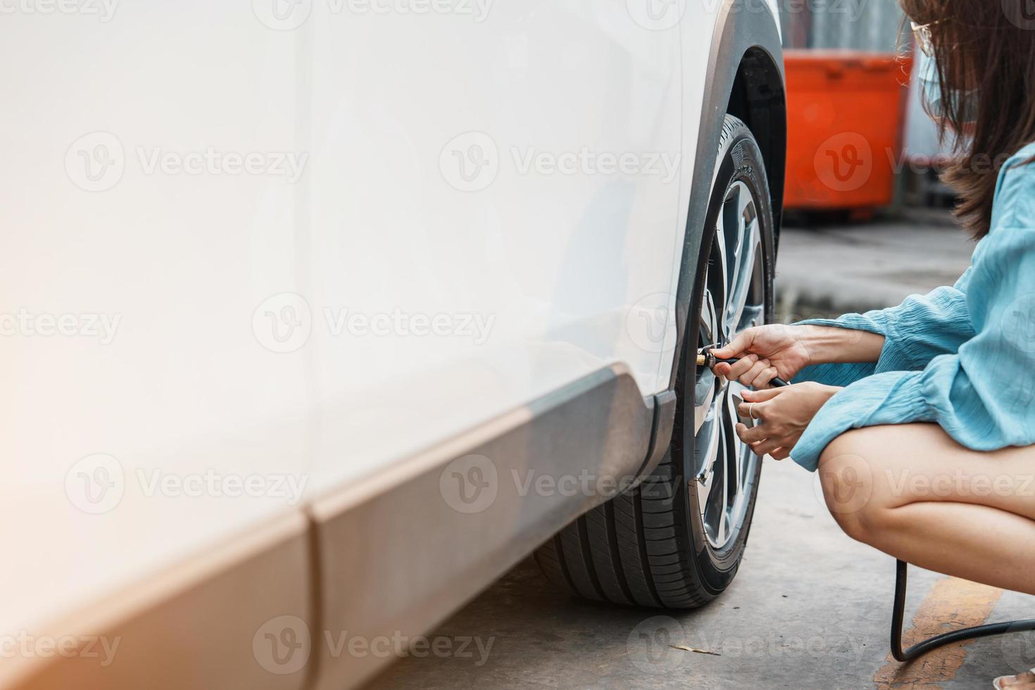 donna conducente che gonfia a mano i pneumatici del veicolo, rimuovendo il tappo di azoto della valvola del pneumatico per controllare la pressione dell'aria e riempire l'aria sulla ruota dell'auto alla stazione di servizio. self service, manutenzione e sicurezza foto