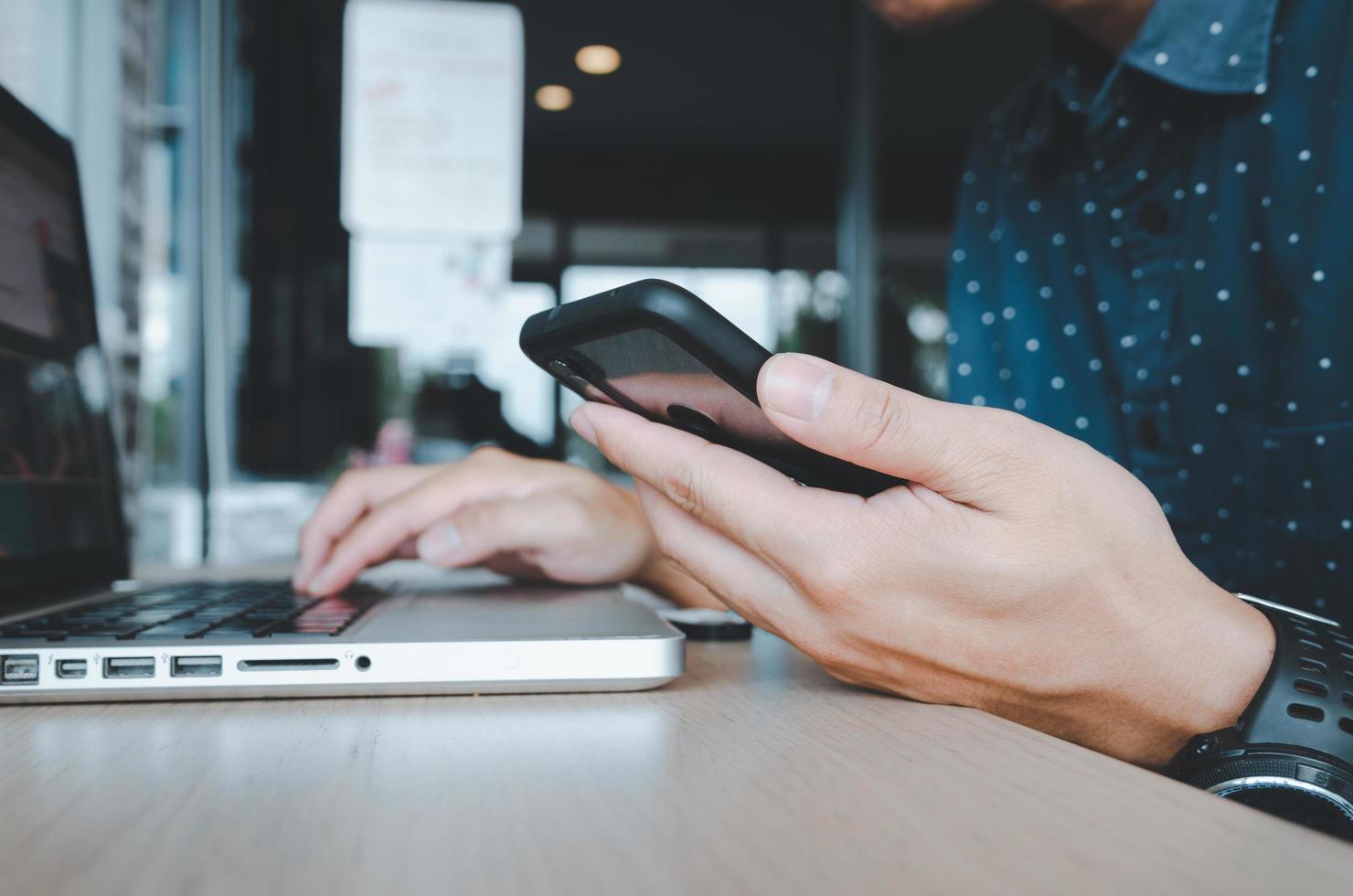 uomo che tiene un telefono cellulare e un computer portatile su una scrivania foto