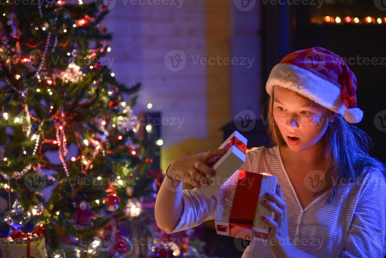il periodo natalizio, una giovane ragazza espressiva che apre la sua confezione regalo foto