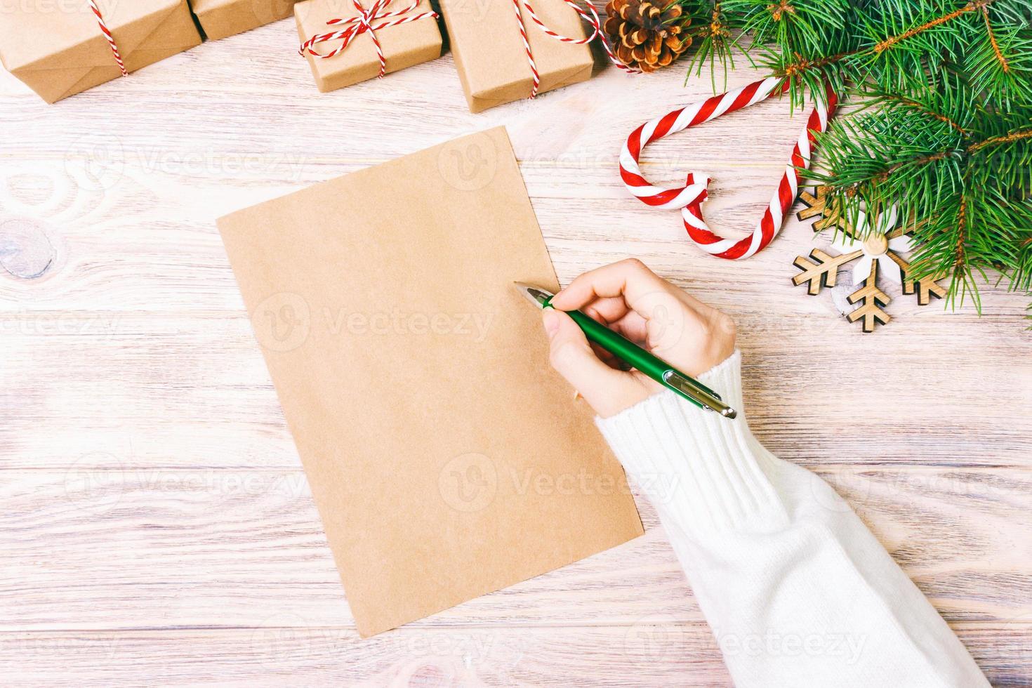 ragazza mano scrittura Natale lettera su mestiere carta con decorazioni su di legno sfondo. tonica foto