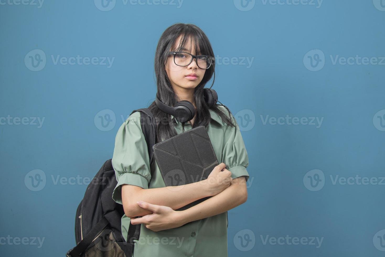 asiatico donna indossare un' verde zaino e Tenere un' tavoletta con cuffie su il sfondo. indietro per scuola e apprendimento concetto. foto