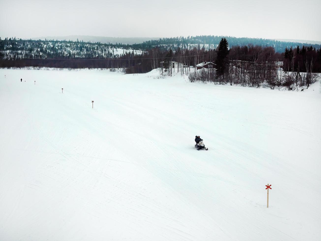 turisti equitazione motoslitte su ghiacciaio attraverso il nevoso montagne nel Finlandia, panoramico scena di bianca neve colline con pino albero. foto