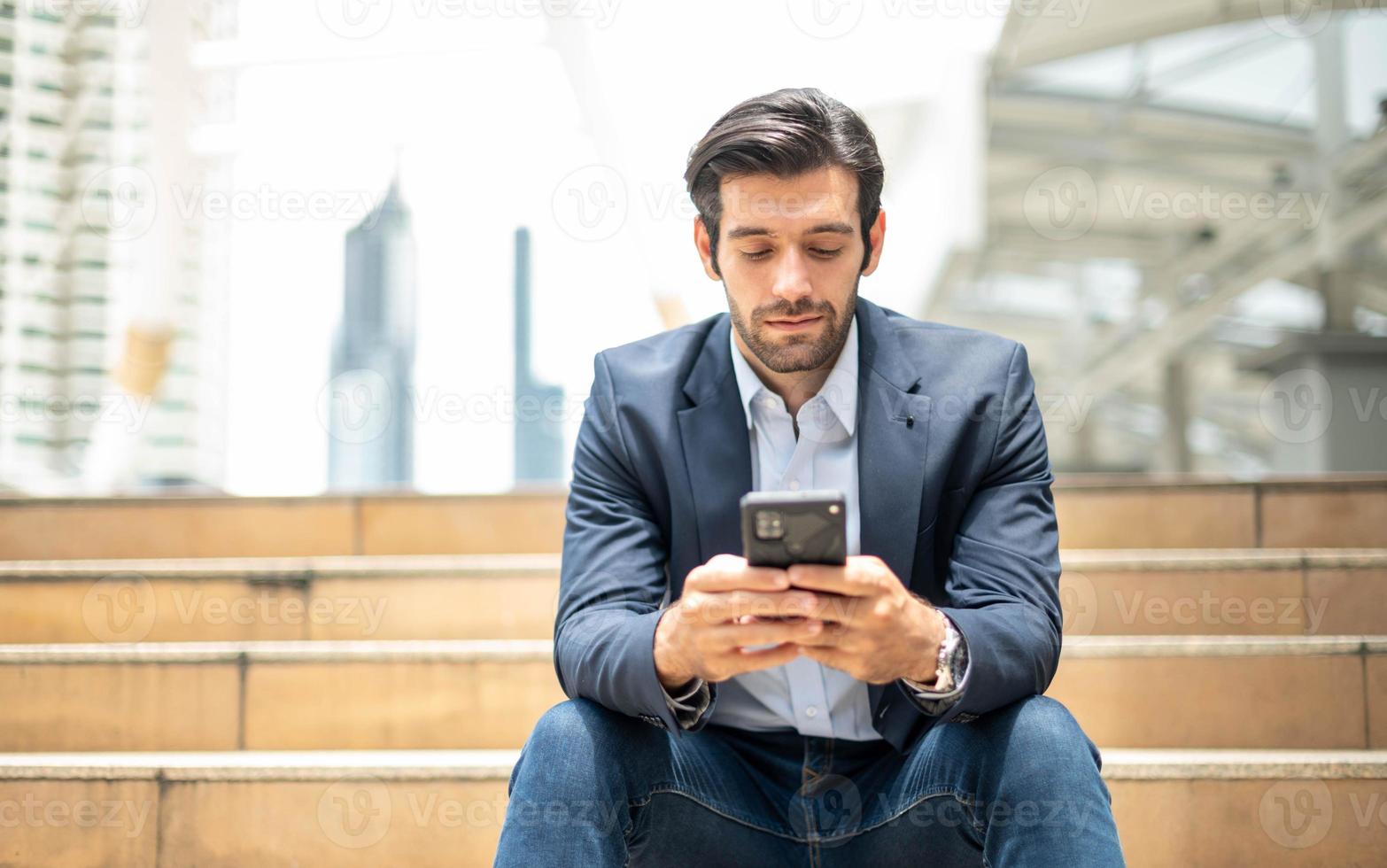 avvicinamento di giovane caucasico grave uomo utilizzando moderno smartphone dispositivo mentre seduta a il pubblico la zona, mentre guardare a il sociale Rete su smartphone. foto