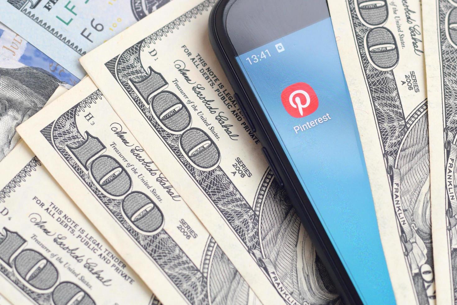 Kharkov, Ucraina - Maggio 3, 2021 smartphone schermo con Pinterest App e lotto di centinaio dollaro fatture. attività commerciale e sociale networking concetto foto