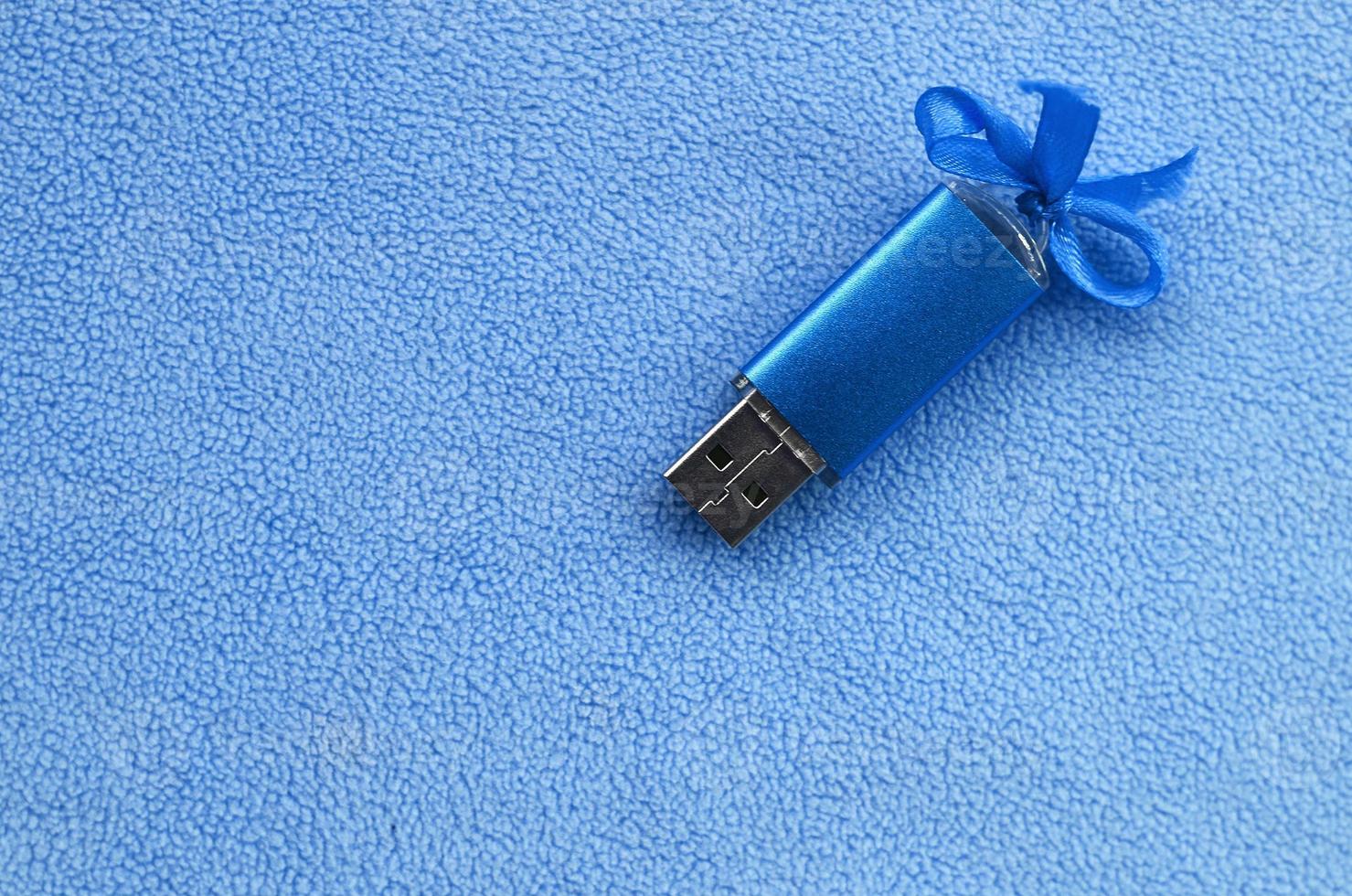 brillante blu USB veloce memoria carta con un' blu arco bugie su un' coperta di morbido e peloso leggero blu vello tessuto. classico femmina regalo design per un' memoria carta foto