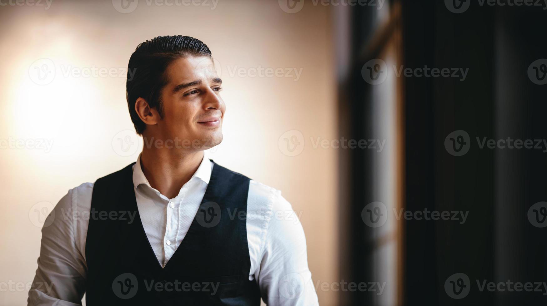 ritratto di un' sorridente caucasico uomo d'affari, in piedi di il finestra e guardare al di fuori foto