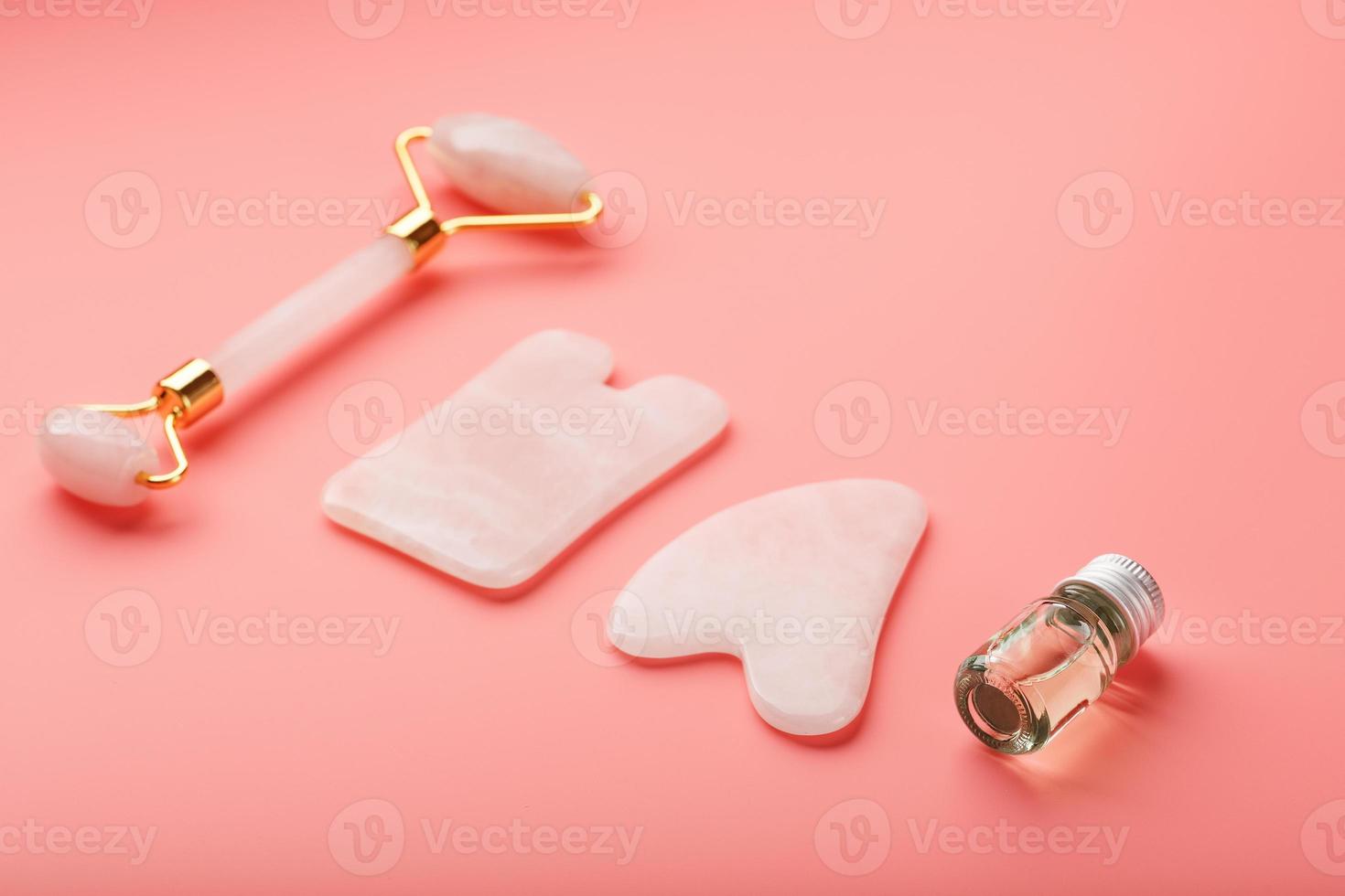 un' impostato di utensili per viso massaggio tecnica gua sha fatto di naturale rosa quarzo su un' rosa sfondo. rullo, giada pietra e olio nel un' bicchiere vaso per viso e corpo cura. foto