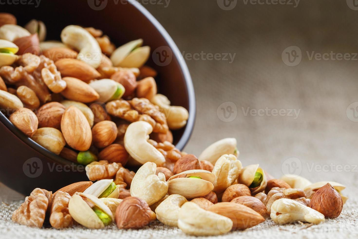 mescolare di diverso noccioline nel un' di legno tazza contro il sfondo di tessuto a partire dal tela. noccioline come struttura e sfondo, macro. superiore Visualizza. foto