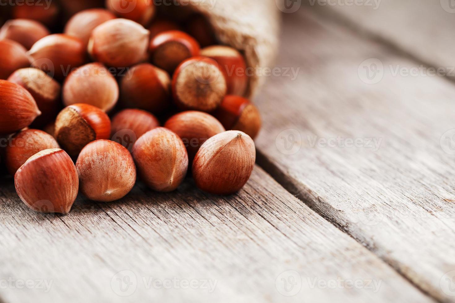 Nocciole nel un' coperchio, versato su a partire dal un' Borsa a partire dal tela ruvida su un' grigio di legno tavolo foto