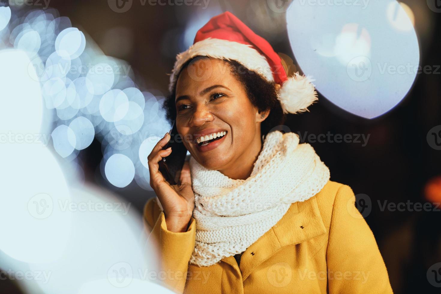 nero donna utilizzando smartphone nel il città a Natale tempo foto