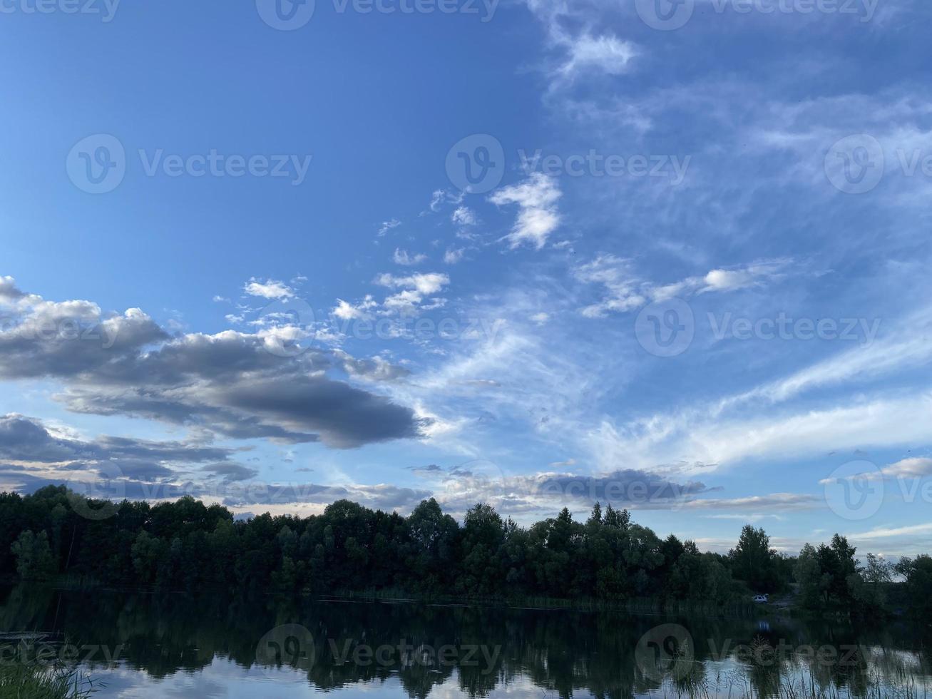 bellissimo tramonto su il lago. tramonto riflessa nel il acqua - blu e arancia cielo con nuvole e alberi nel silhouette foto