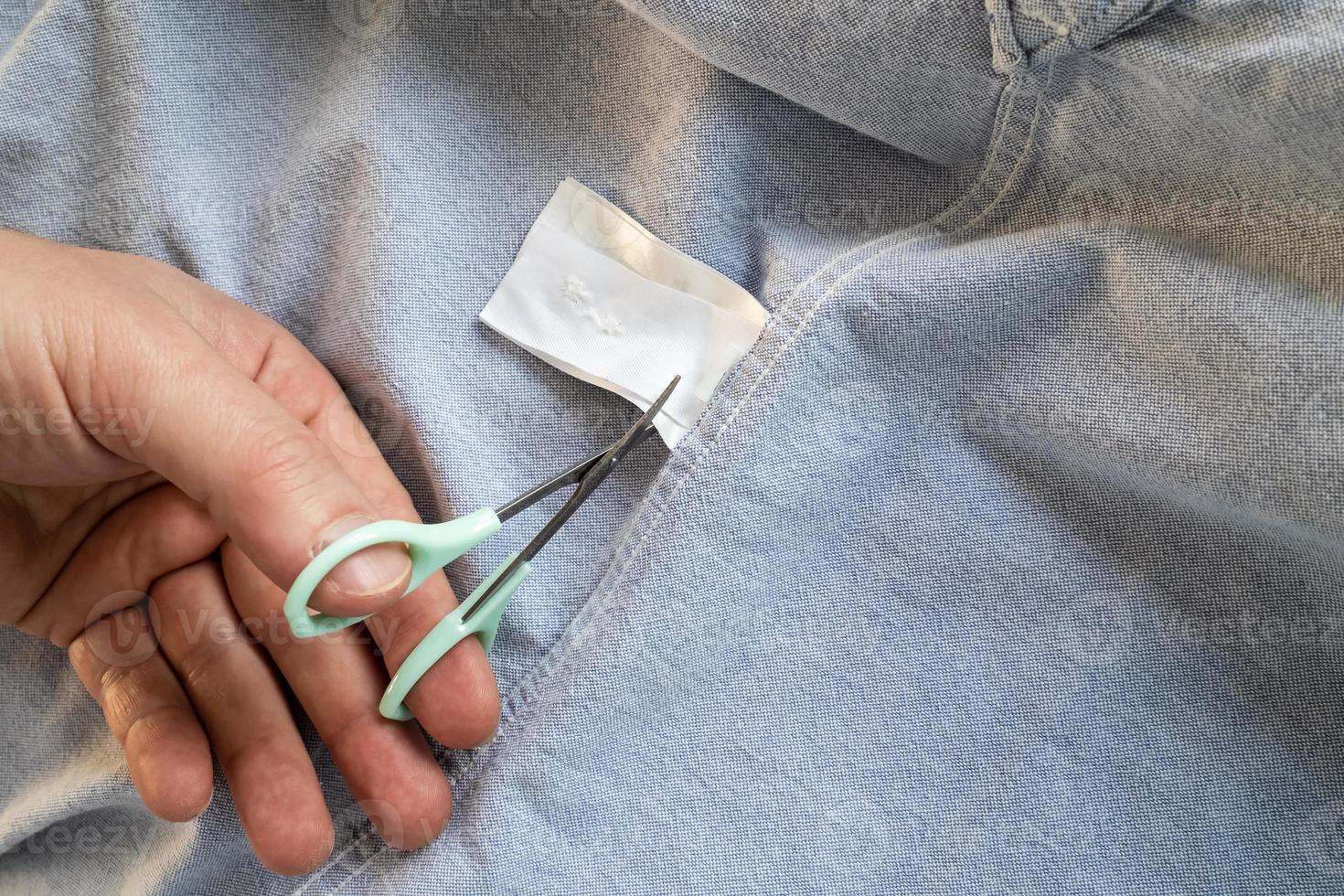 mano tagli via il istruzione etichetta con forbici su un' nuovo camicia, grigio. copia spazio. flatley. foto