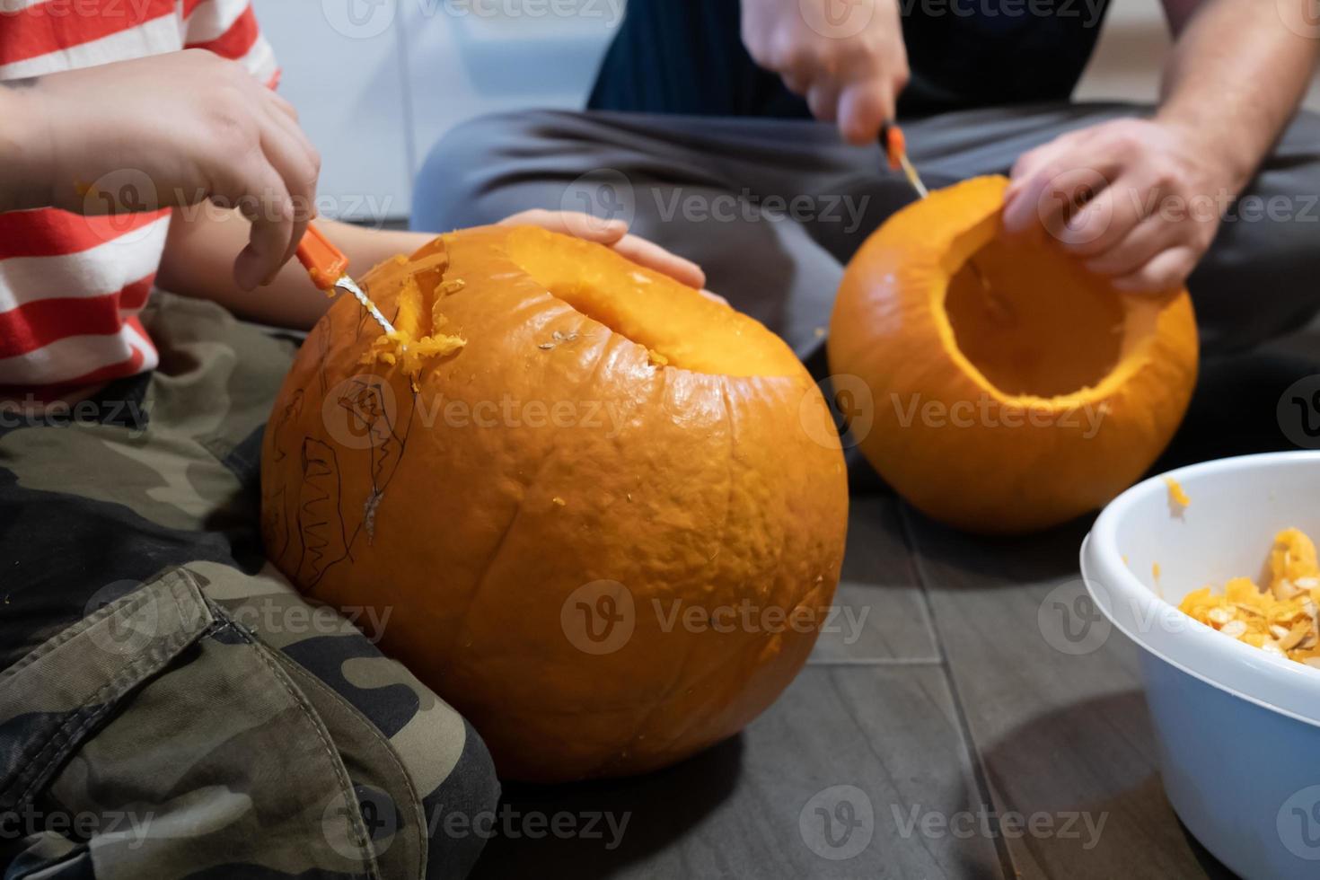 Halloween preparazione. famiglia intaglio zucca in jack-o-lanterna mentre seduta su il pavimento, nel il Casa. foto