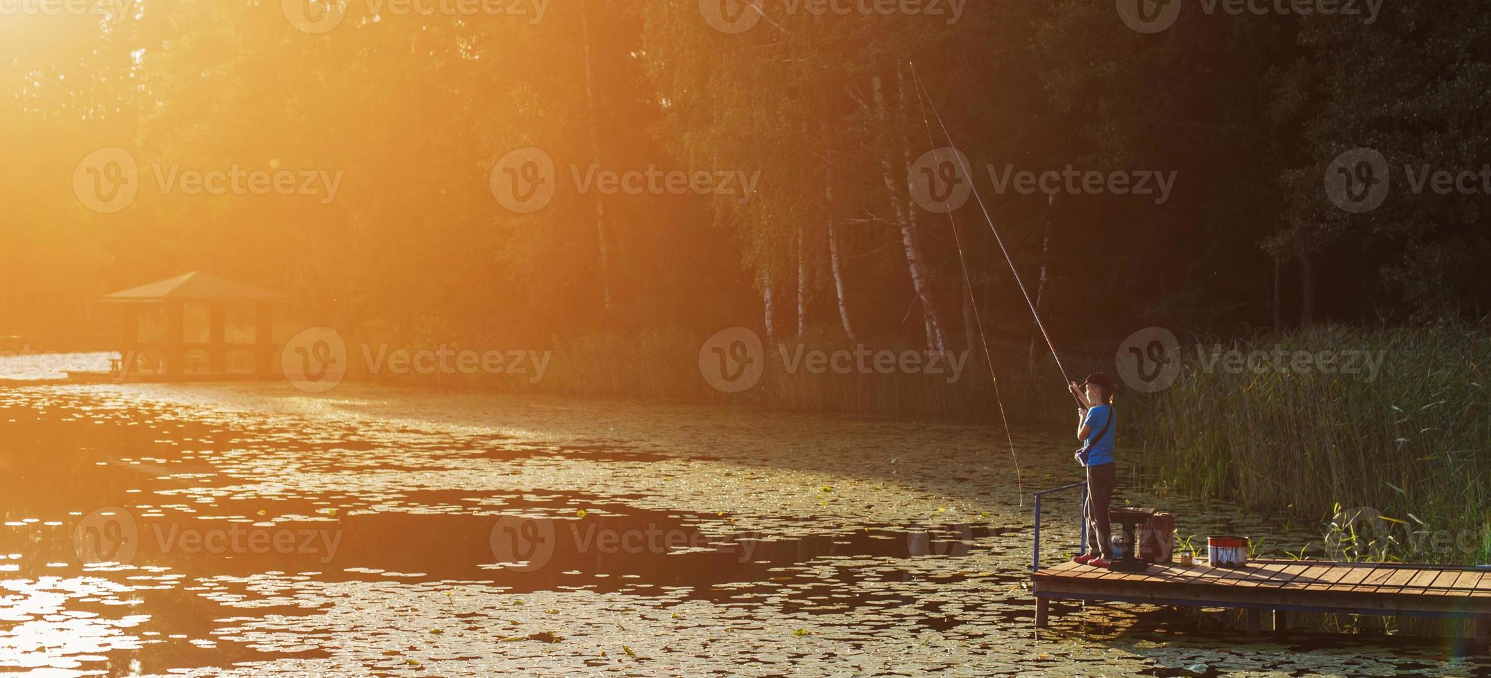 poco ragazzo in piedi e pesca su un' di legno bacino a il tramonto foto