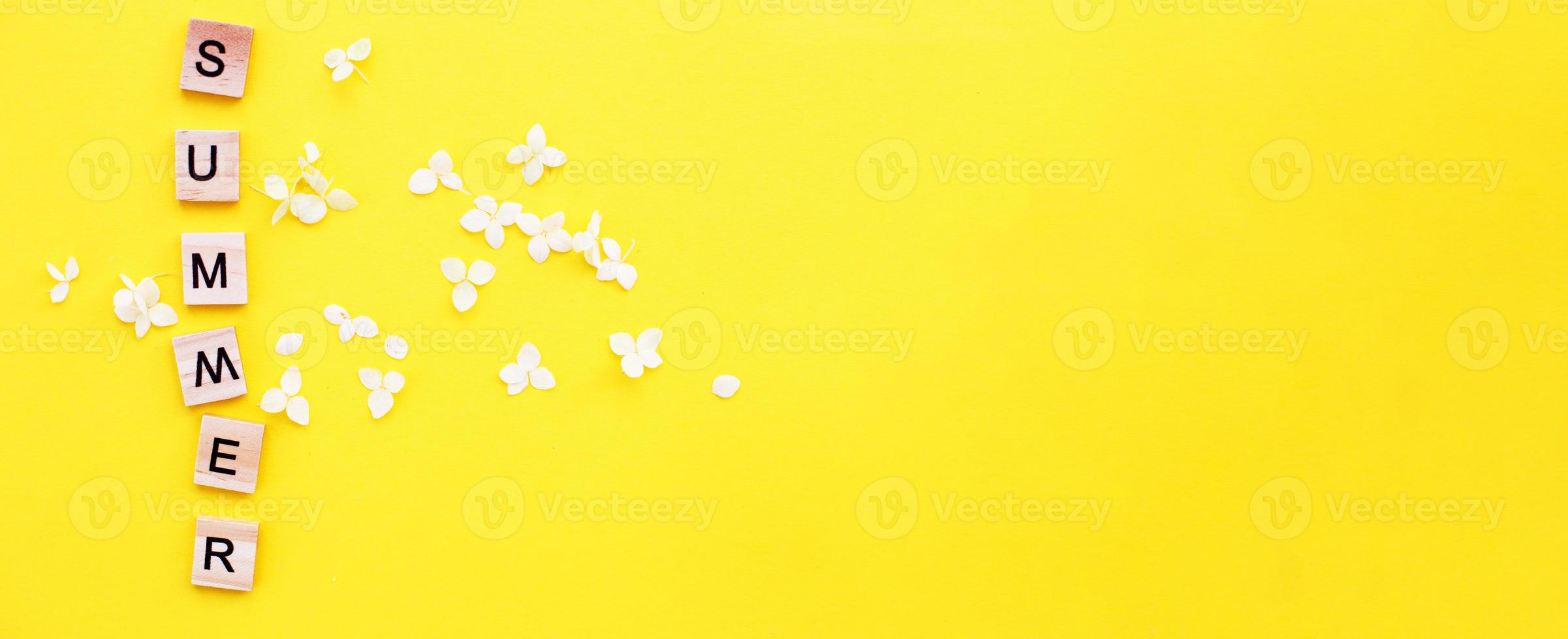 parola estate scritto a partire dal un' di legno cubi con lettere su giallo sfondo con un' petali di un' ortensia fiori foto