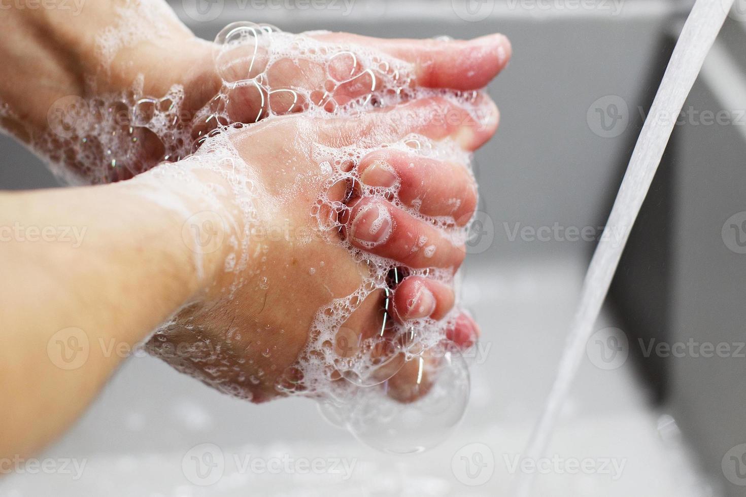 un' uomo lavaggi il suo mani con sapone sotto il rubinetto sotto in esecuzione acqua avvicinamento. Salute, e igiene concetto. foto