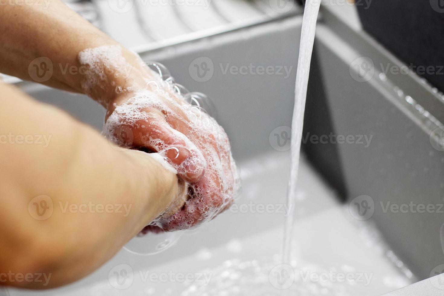 un' uomo lavaggi il suo mani con sapone sotto il rubinetto sotto in esecuzione acqua avvicinamento. Salute, e igiene concetto. foto