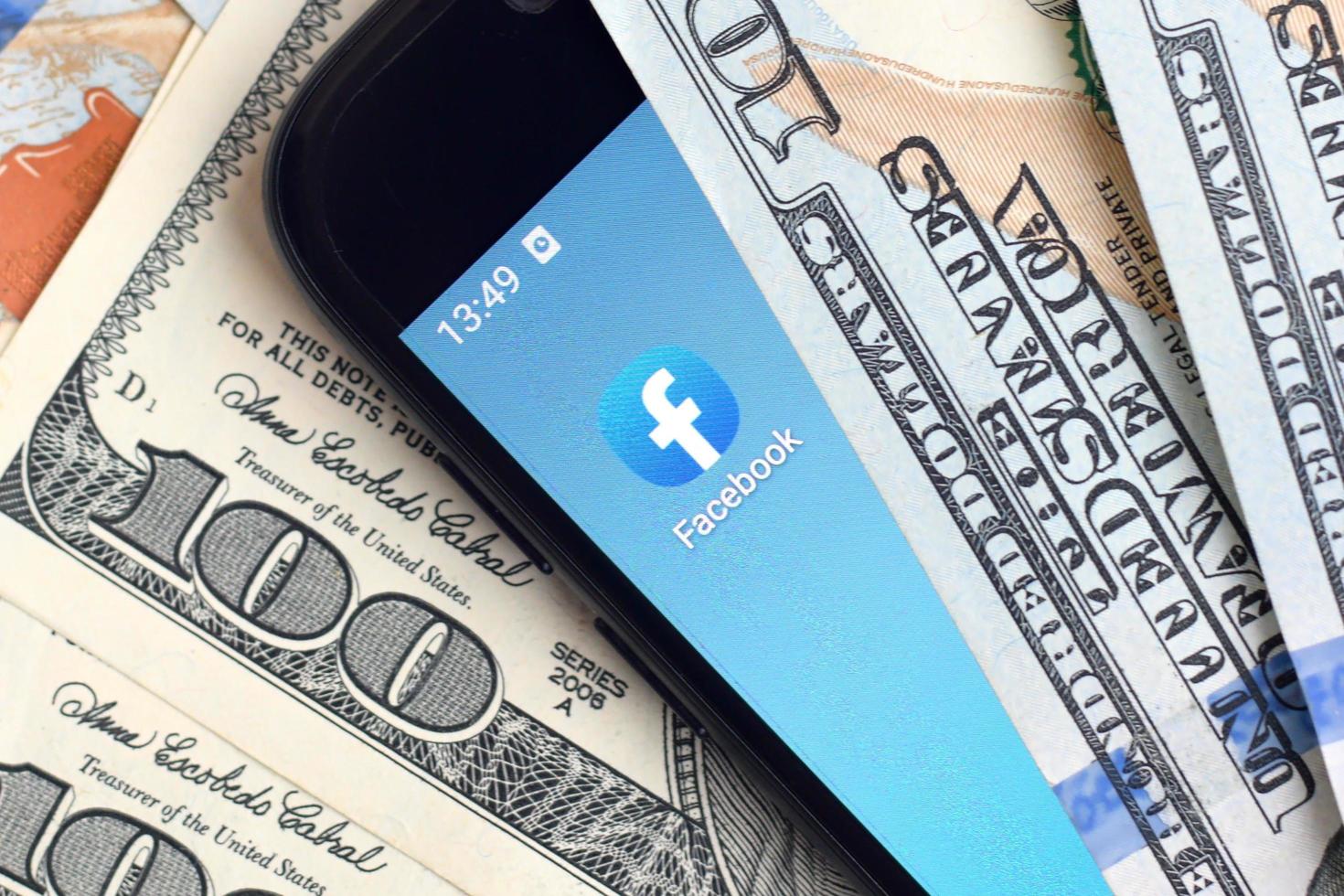 Kharkov. Ucraina - Maggio 17, 2022 smartphone schermo con Facebook App e lotto di centinaio dollaro fatture. attività commerciale e sociale networking concetto foto