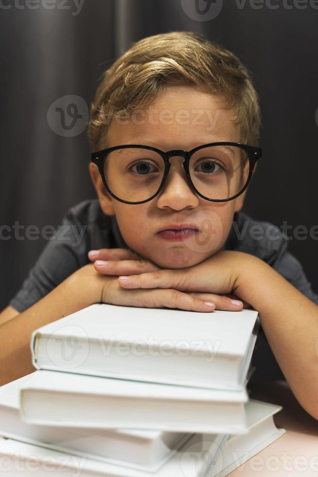 un' ragazzo con bicchieri e un' pila di libri, indietro per scuola, studia fatica, studia le difficoltà foto