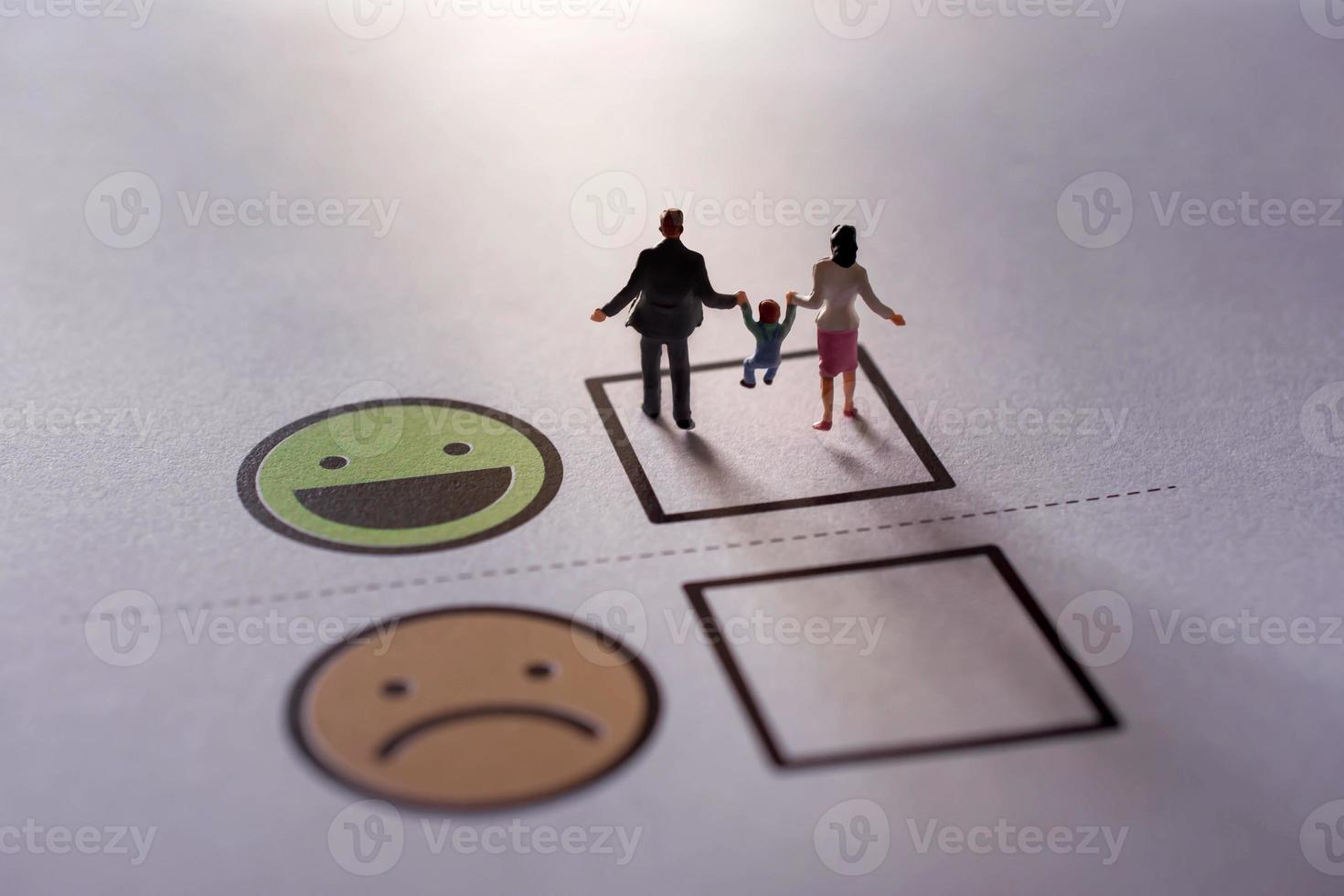 contento famiglia cliente concetto. presente di miniatura figura di padre, madre e figlio nel felicità momento. a piedi su un' verificato scatola di smiley cartone animato viso foto