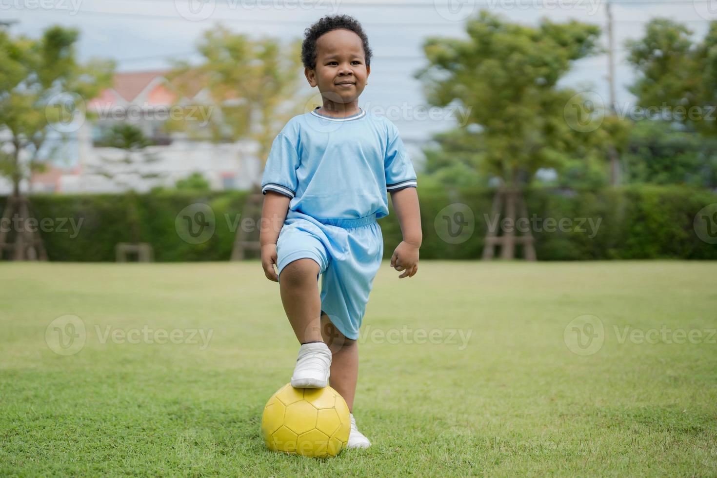 carino poco ragazzo con calcio palla nel il parco su un' soleggiato giorno. foto