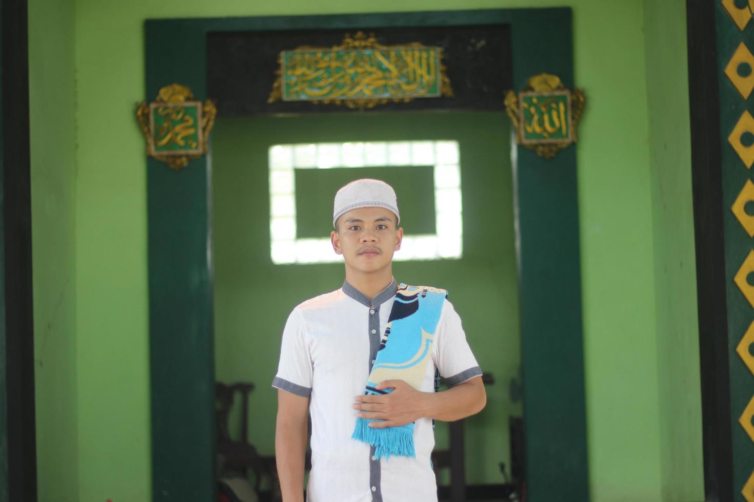 giovane asiatico musulmano preghiere nel il moschea trasporto un' preghiera stuoia foto