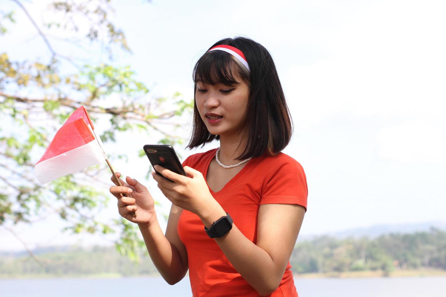 bellissimo giovane asiatico donna trasporto il indonesiano bandiera con un' allegro viso e chiamata il suo amico foto