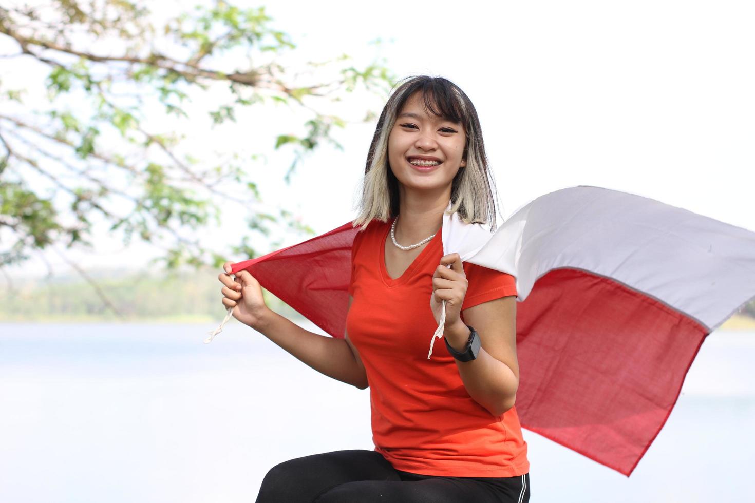 bellissimo giovane asiatico donna trasporto il indonesiano bandiera con un' allegro viso foto