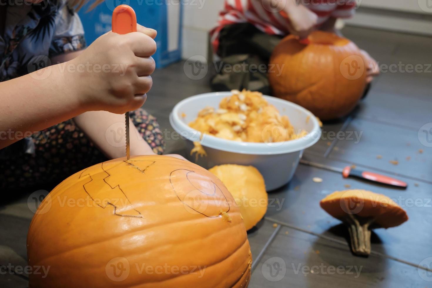 Halloween preparazione. famiglia intaglio zucca in jack-o-lanterna mentre seduta su il pavimento, nel il Casa. foto