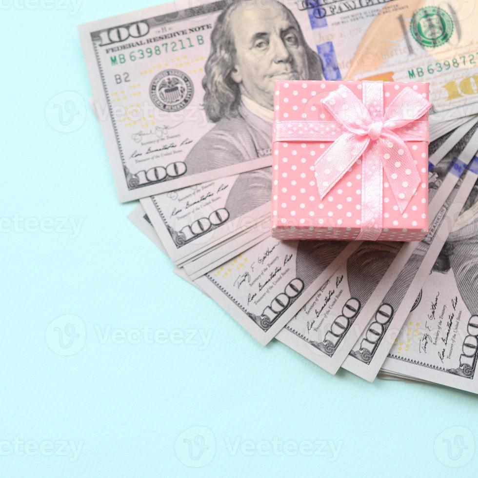rosa tratteggiata regalo scatola bugie vicino centinaio dollaro fatture su un' leggero blu sfondo foto