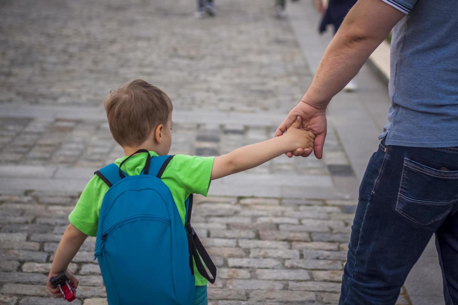 un' padre detiene il suo figli maschi mano mentre a piedi giù un' città strada. viaggio. stile di vita nel il città. centro, strade. foto