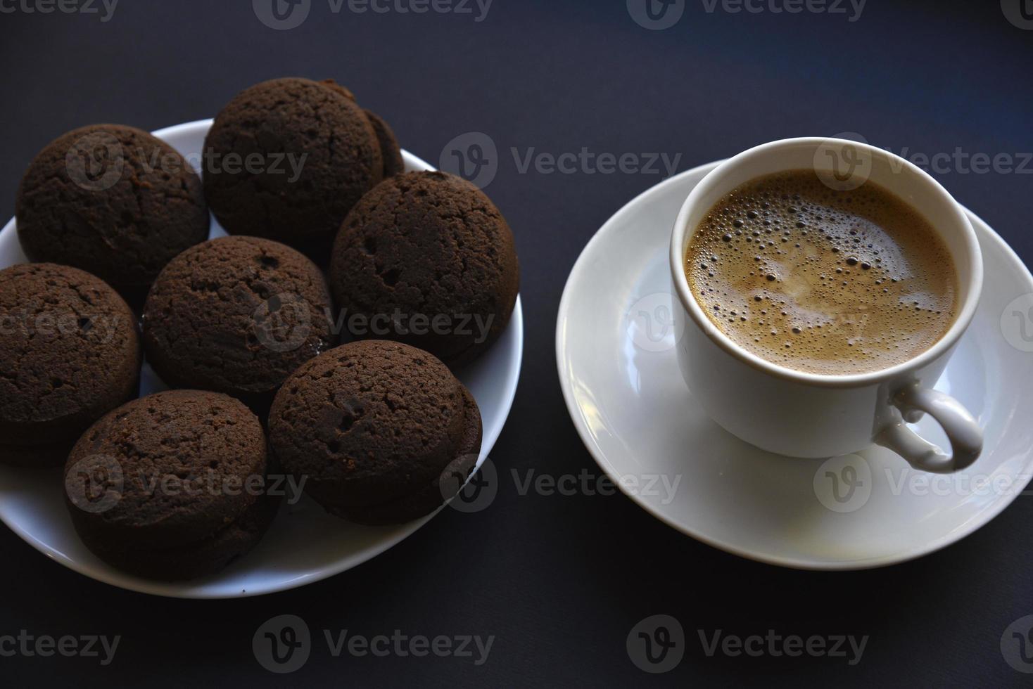 delizioso nero caffè con schiuma nel un' bianca tazza con dolce biscotti. delizioso prima colazione con caffè e biscotti. dolce e morbido biscotti su un' nero sfondo. foto