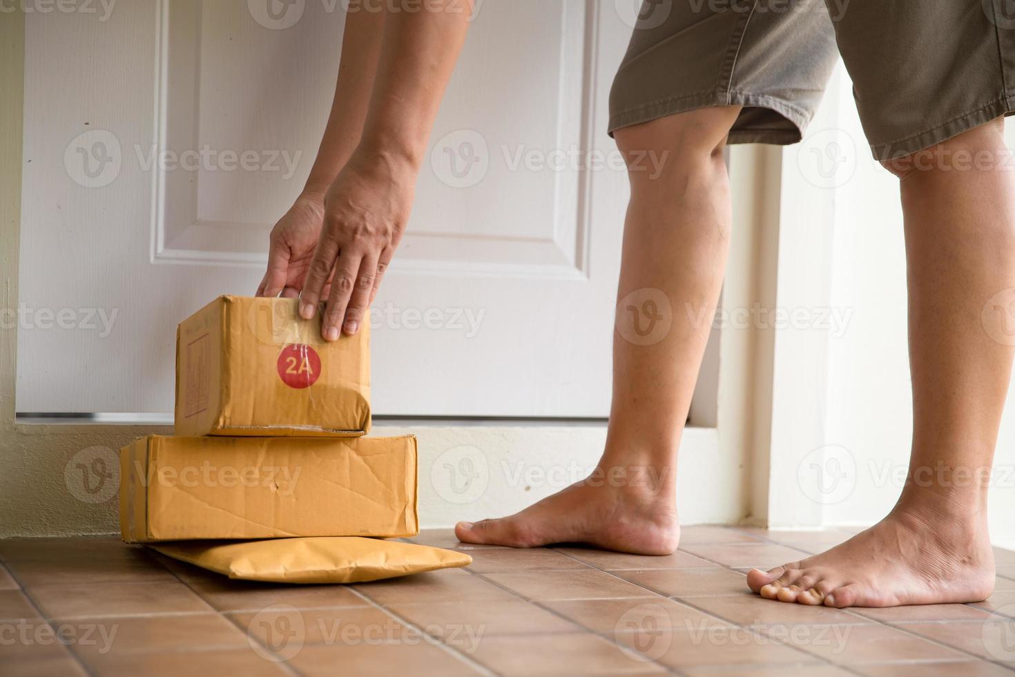 donna raccoglie pacco a porta. scatola vicino porta su pavimento. in linea acquisti, scatole consegnato per il tuo davanti porta. facile per rubare quando nessuno è casa. pacco nel cartone scatola su porta di casa. consegna servizio foto