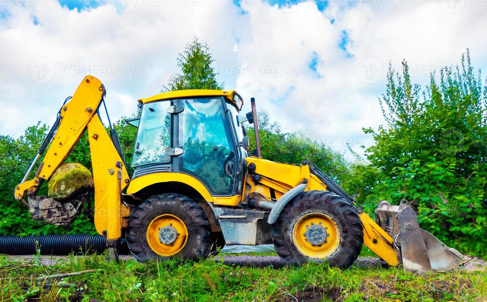 parcheggiata grande giallo multifunzionale ruota trattore su il radura contro verde alberi nel soleggiato giorno. giallo terna foto