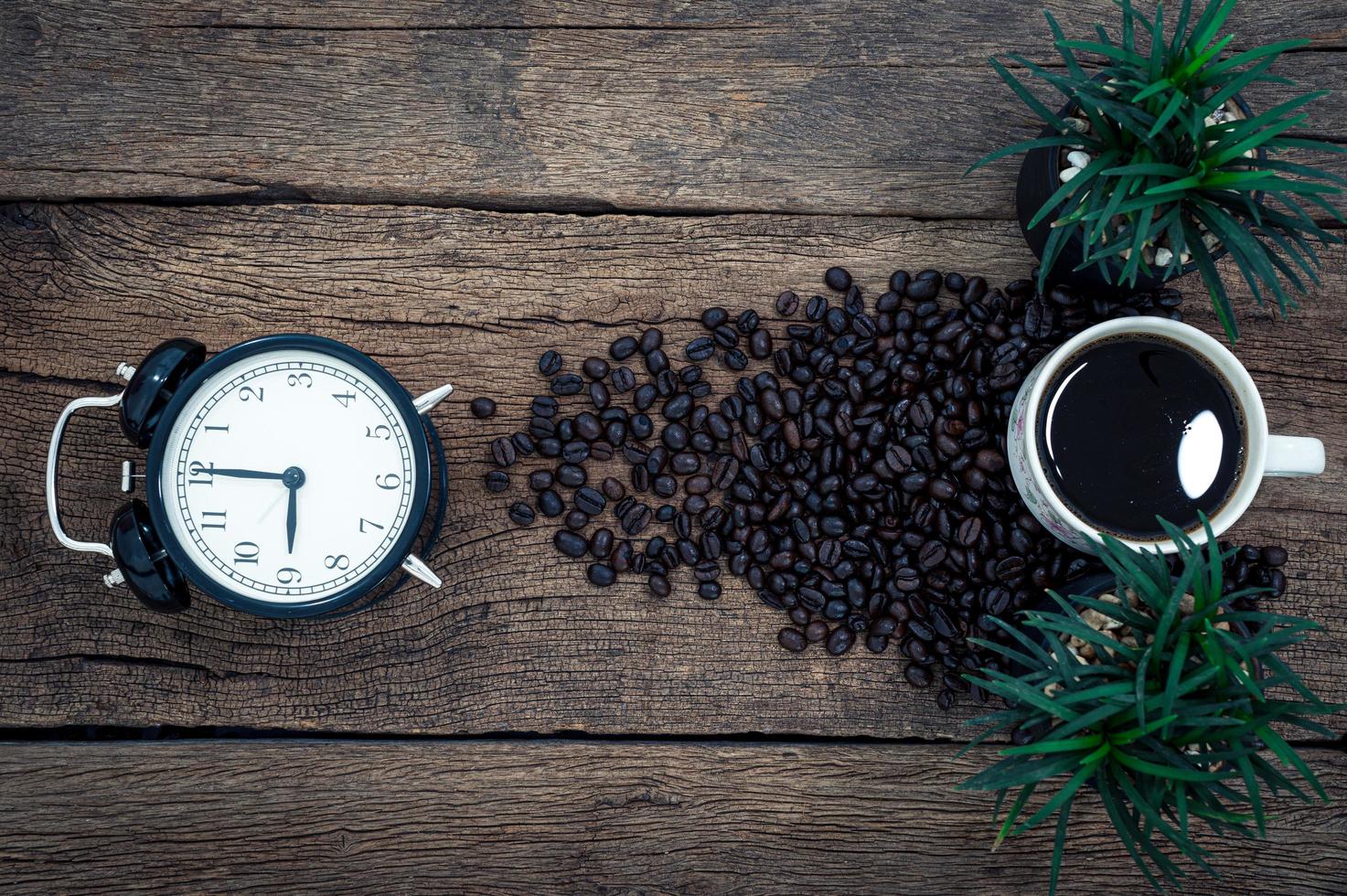 sveglia, tazza di caffè e chicchi di caffè sulla scrivania foto