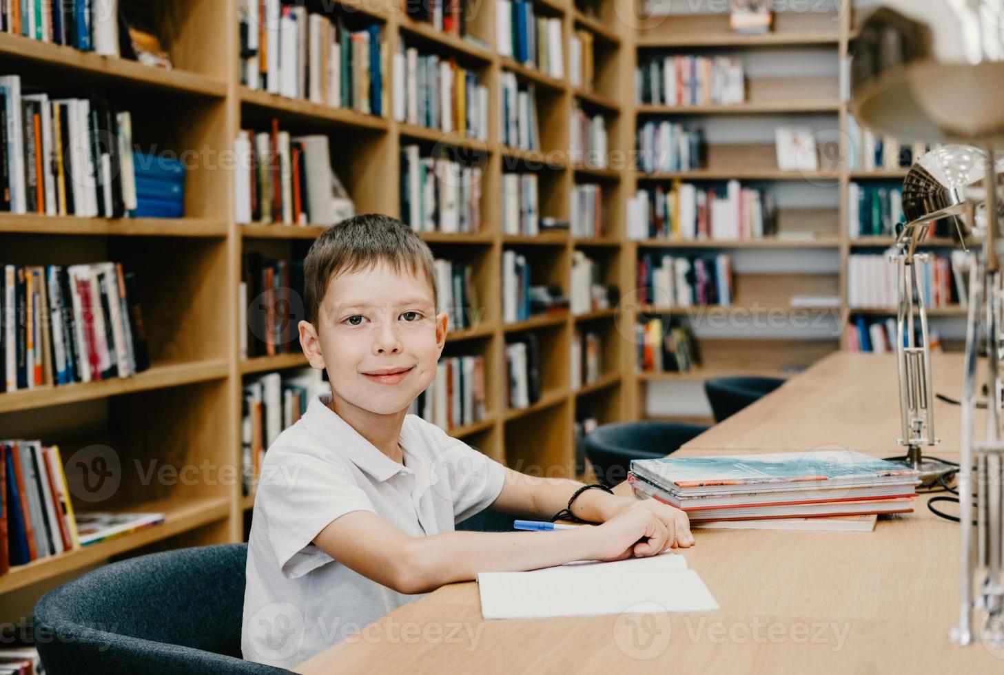 il ragazzo si siede nel il biblioteca e scrive nel un' taccuino a il tavolo. preparazione per compiti a casa. un' bene alunno. scolaro gli amori per studia. gratuito spazio a scuola. foto