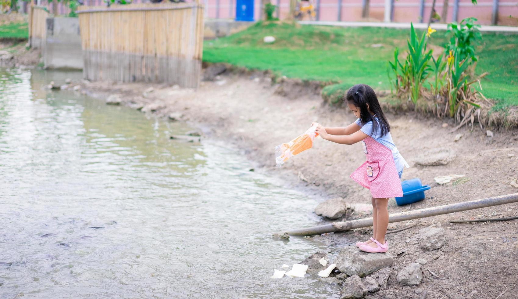 una bambina che alimenta i pesci allo stagno in un parco pubblico foto