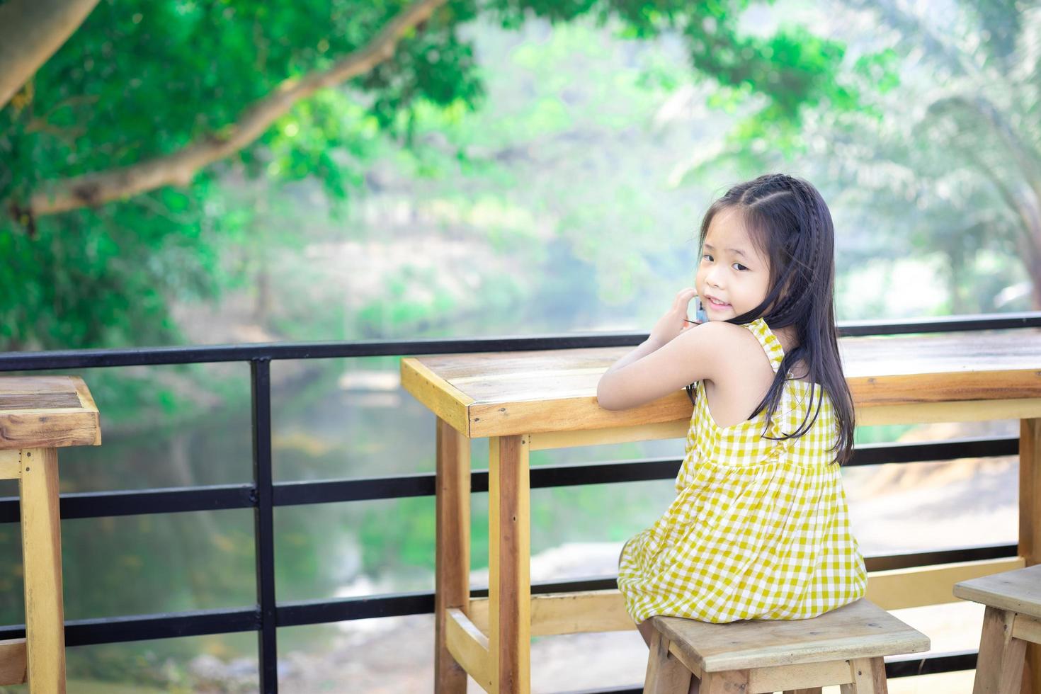 piccola ragazza asiatica che si siede sulla sedia a un tavolo di legno foto