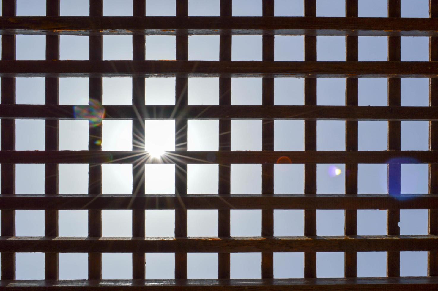 struttura di un' Marrone di legno astratto reticolo con piazza cellule con fori di tavole di log travi disposte verticalmente orizzontalmente contro il sfondo di il sole e cielo. il sfondo foto