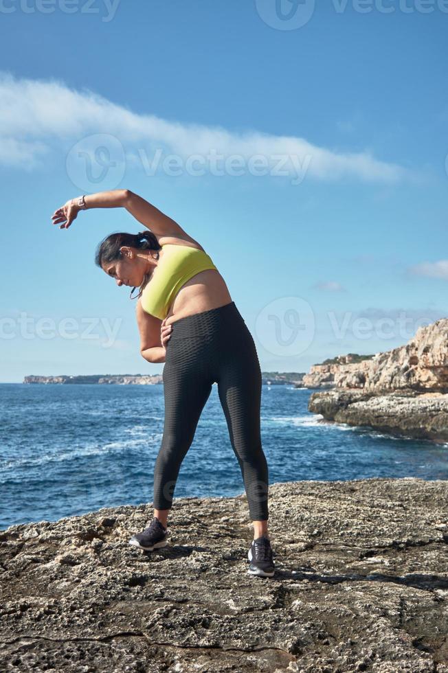 latino donna, di mezza età, indossare abbigliamento sportivo, addestramento, fare fisico esercizi, tavola, sit-up, quello dello scalatore fare un passo, ardente calorie, conservazione in forma, all'aperto di il mare, indossare cuffia, inteligente orologio foto