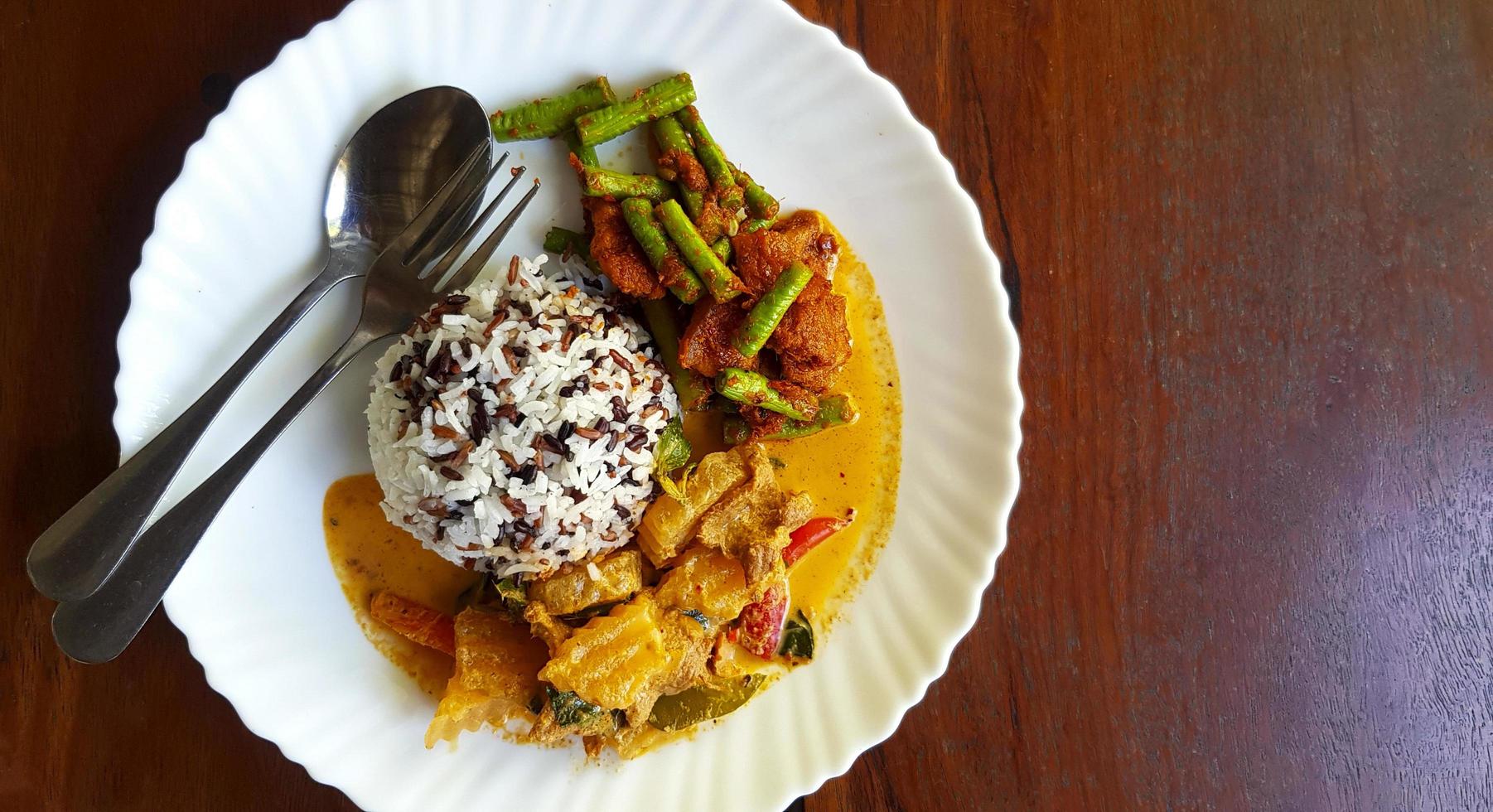 superiore Visualizza di tre colore riso con speziato giallo curry con Maiale e agitare fritte Maiale pancia e rosso curry incolla con corda fagiolo nel bianca piatto su Marrone di legno sfondo o tavolo con copia spazio. foto