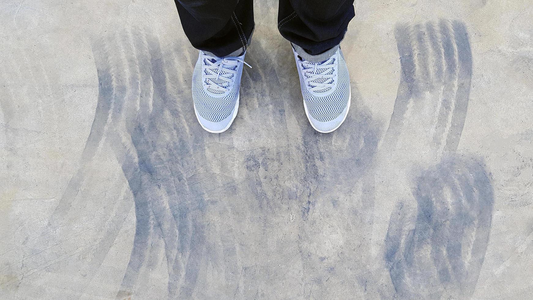 superiore Visualizza di gamba indossare blu jeans e grigio o grigio scarpe da ginnastica o moda scarpe su pavimento con auto ruota o freno marchio su strada o strada con copia spazio. piatto posare di parte corpo. astratto sfondo foto